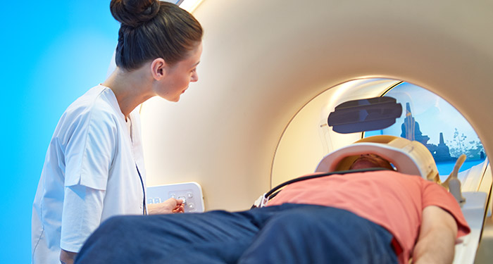 una donna che guarda un uomo disteso in una macchina per la scansione TC